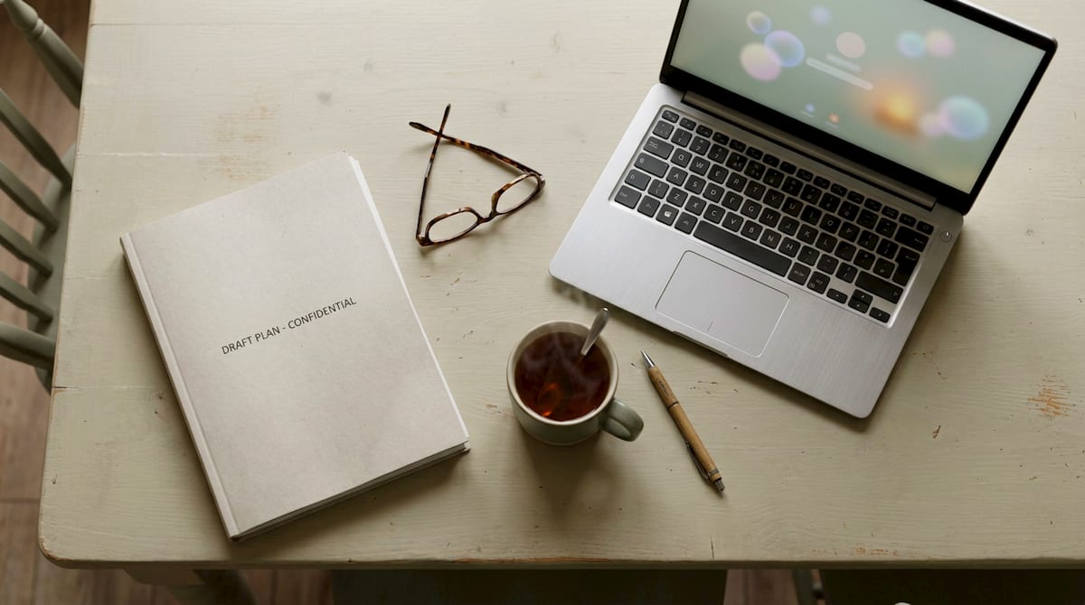 A draft plan document, reading glasses and a laptop laid out on a table to check the wording carefully. AI-generated illustration.
